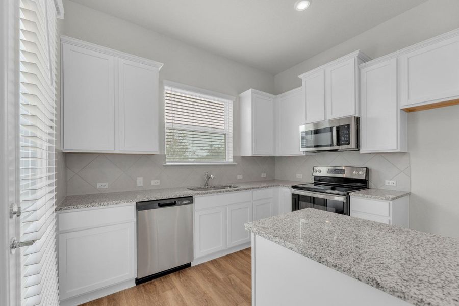 Kitchen with appliances with stainless steel finishes, white cabinetry, light wood-style flooring, light stone countertops, and recessed lighting