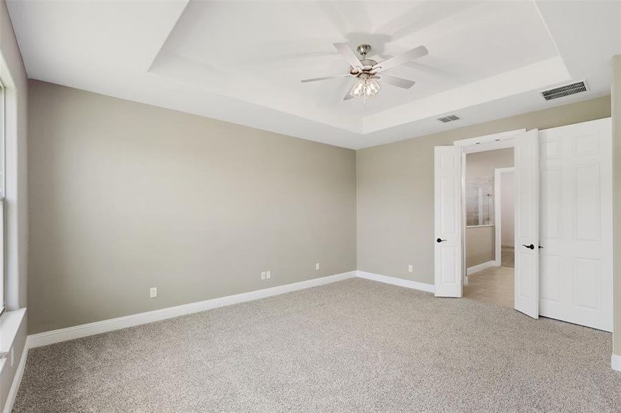 Unfurnished bedroom featuring ceiling fan, carpet floors, and a tray ceiling