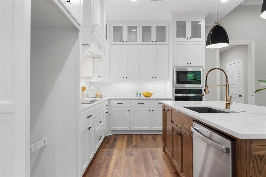 Kitchen with a sink, dark wood finished floors, stainless steel appliances, pendant lighting, and glass insert cabinets