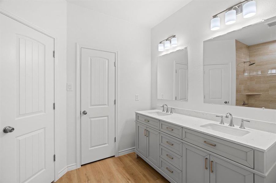 Bathroom featuring double vanity, wood finished floors, and tiled shower Bathroom featuring double vanity, wood finished floors, and tiled shower