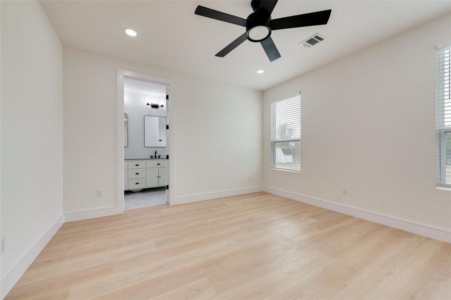 Unfurnished bedroom featuring ensuite bath, ceiling fan, and light wood-type flooring