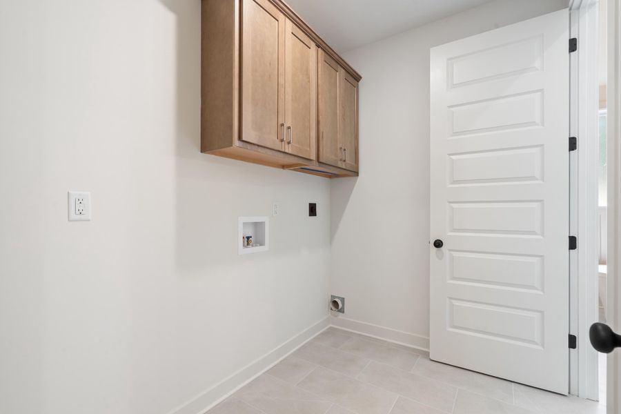 Light-toned wall cabinetry, light grey tile flooring, white paneled door, and matte black door hardware Light-toned wall cabinetry, light grey tile flooring, white paneled door, and matte black door hardware
