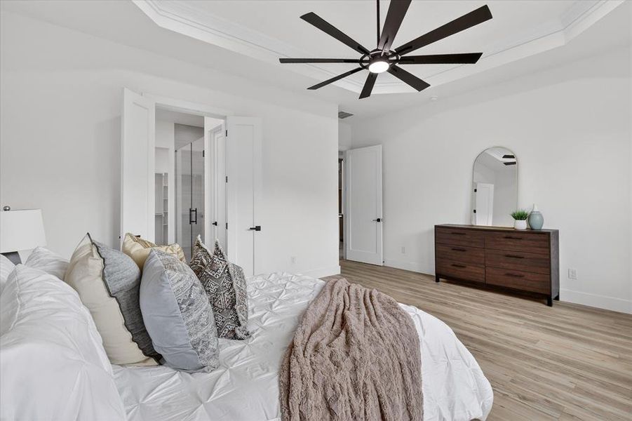 Bedroom featuring a raised ceiling, arched walkways, ceiling fan, light wood finished floors, and ensuite bath