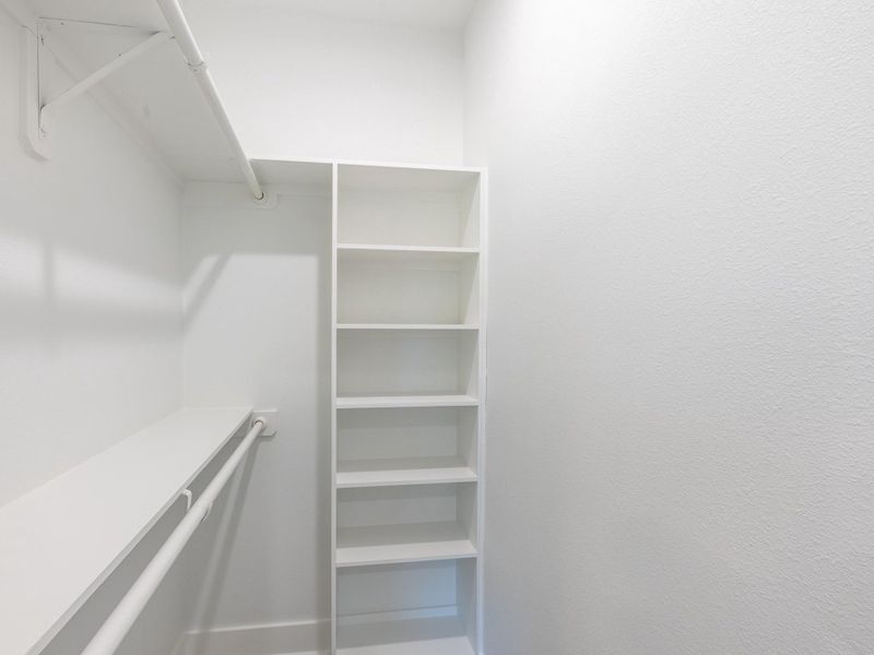 This is a spacious walk-in closet with white walls, featuring built-in shelves and a hanging rod, providing ample storage space.