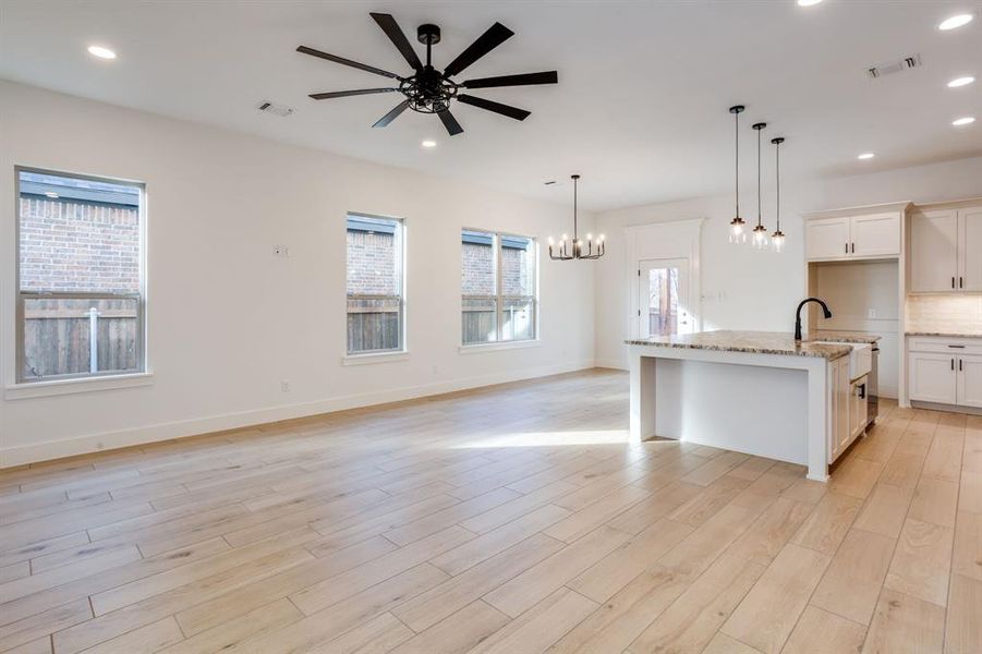 Kitchen featuring an island with sink, open floor plan, light stone counters, a chandelier, and light wood finished floors