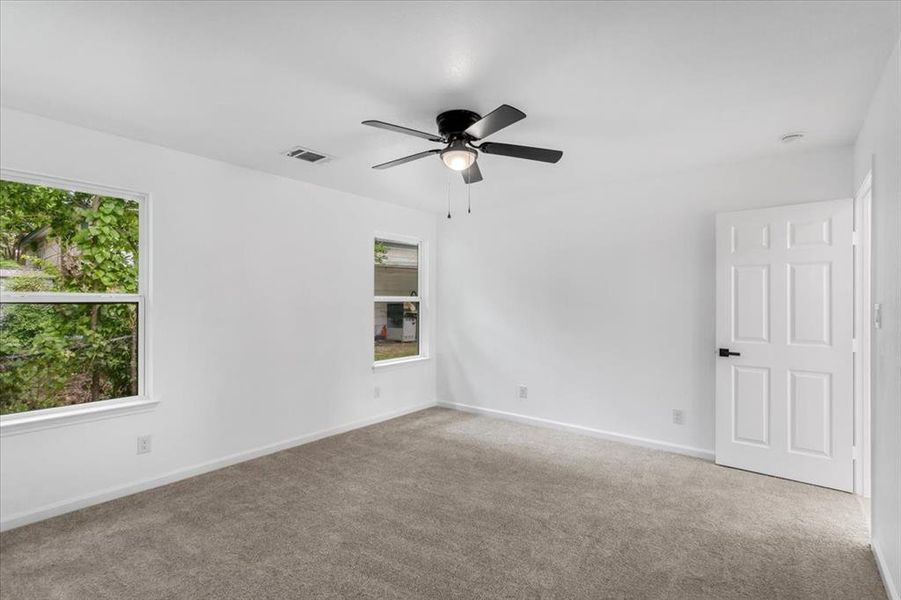 Carpeted master bedroom with a wealth of natural light and ceiling fan