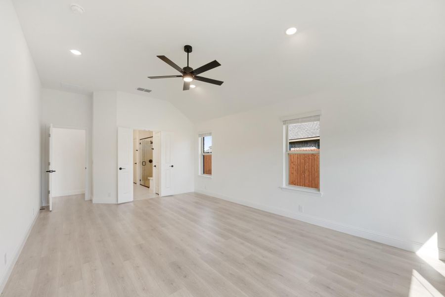 Spacious master bedroom with vaulted ceiling, ceiling fan, light wood floors, and ensuite bathroom entrance