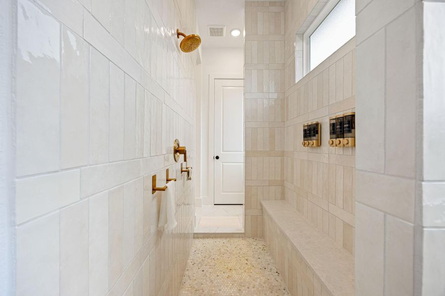 Primary walk-through shower with sleek tiles, a built-in bench, and gold fixtures, providing a luxurious and elegant bathroom experience.