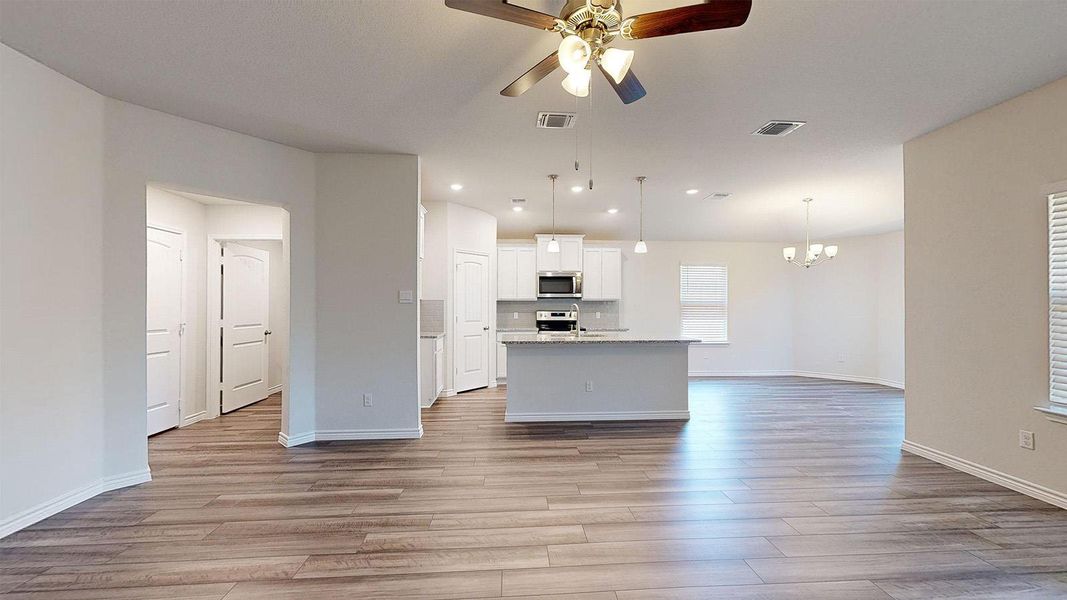 Kitchen featuring open floor plan, a ceiling fan, a center island with sink, white cabinetry, and hanging lights Kitchen featuring open floor plan, a ceiling fan, a center island with sink, white cabinetry, and hanging lights