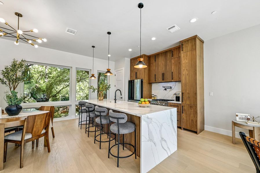 Kitchen featuring custom wood cabinets, quartz waterfall countertop with breakfast bar area, and high end stainless steel appliances. (This is Unit #2 - each Unit has the same layout, however a few differing details such as light fixtures, custom cabinet/backsplash/tile colors)