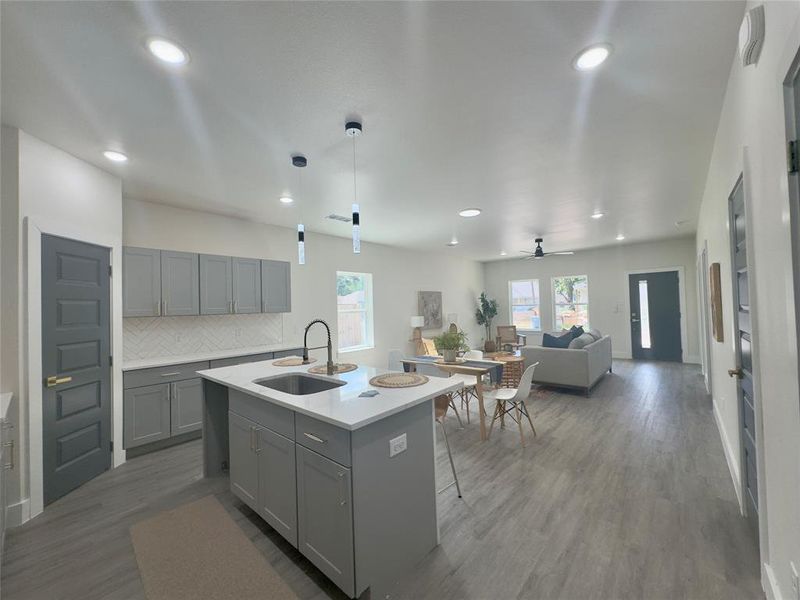 Kitchen featuring a center island with sink, wood-type flooring, backsplash, hanging light fixtures, and sink