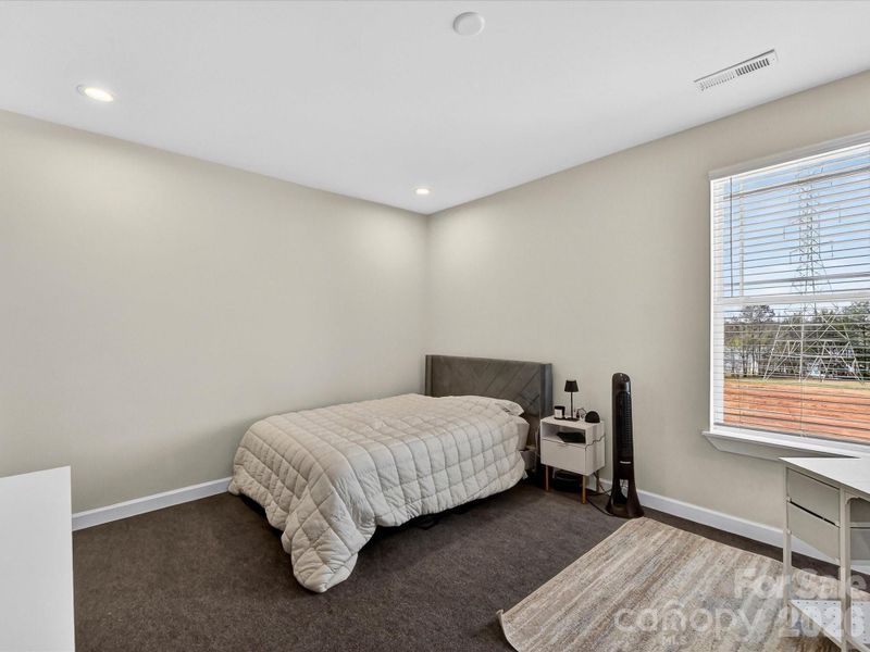 Bright and simple bedroom featuring neutral tones, cozy carpeting, and a large window for natural light.