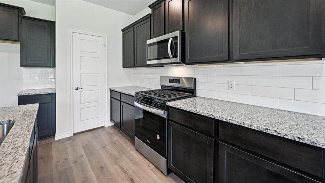 Kitchen featuring stainless steel appliances, light stone countertops, light wood-style floors, and tasteful backsplash