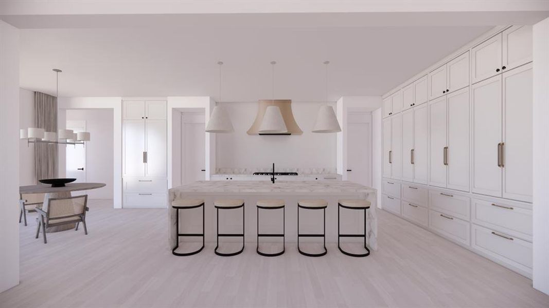 Kitchen with light stone counters, decorative light fixtures, a center island with sink, white cabinetry, and premium range hood