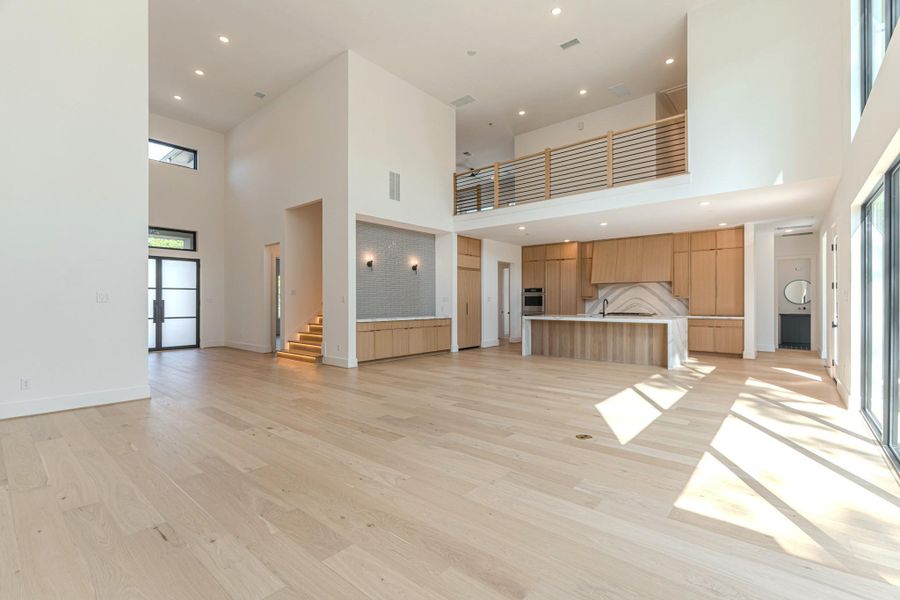 This photo showcases a spacious, modern open-plan living area with high ceilings and abundant natural light. It features light wood flooring, a stylish kitchen with wood cabinetry and a large island, and a mezzanine level. The space is airy and contemporary, ideal for both relaxation and entertaining.