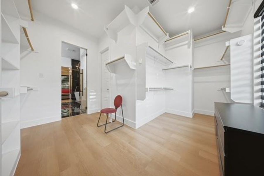 Expansive walk-in closet featuring light wood-finish flooring, recessed lighting, custom built-in shelving, and hanging rods