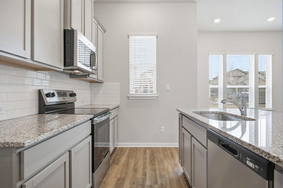 Kitchen with stainless steel appliances, gray cabinetry, light stone countertops, light wood finished floors, and plenty of natural light