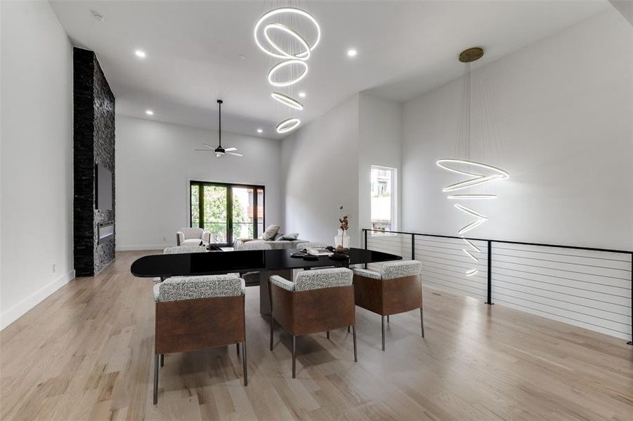 Dining space featuring light wood-type flooring, ceiling fan, a chandelier, recessed lighting, and a high ceiling