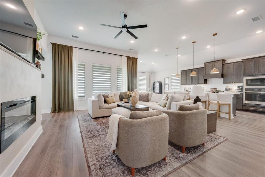 Open-concept living space featuring wood-finish flooring, a modern electric fireplace, recessed lighting, and a kitchen with stainless steel appliances and pendant lights