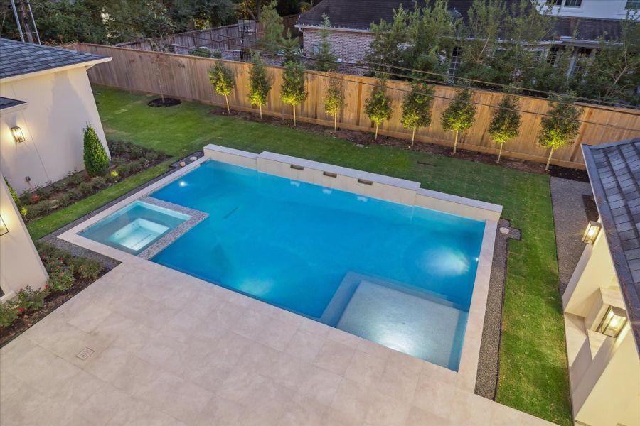 Expansive backyard with a modern pool and flushed spa, surrounded by wide stone decking ideal for lounging and entertaining.