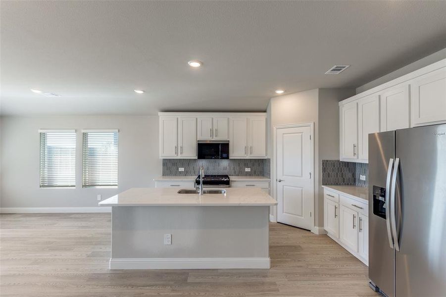 Kitchen with stainless steel appliances, a center island with sink, light stone counters, white cabinetry, and recessed lighting