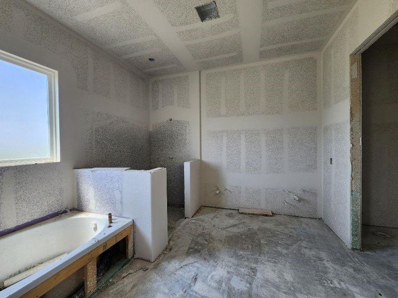 Spacious bathroom under construction, featuring a built-in tub, a large window, drywall-finished walls, and ceiling with recessed lighting potential
