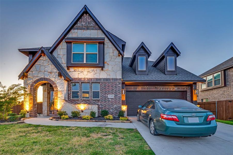 View of front facade with concrete driveway, stone siding, a garage, roof with shingles, and brick siding View of front facade with concrete driveway, stone siding, a garage, roof with shingles, and brick siding