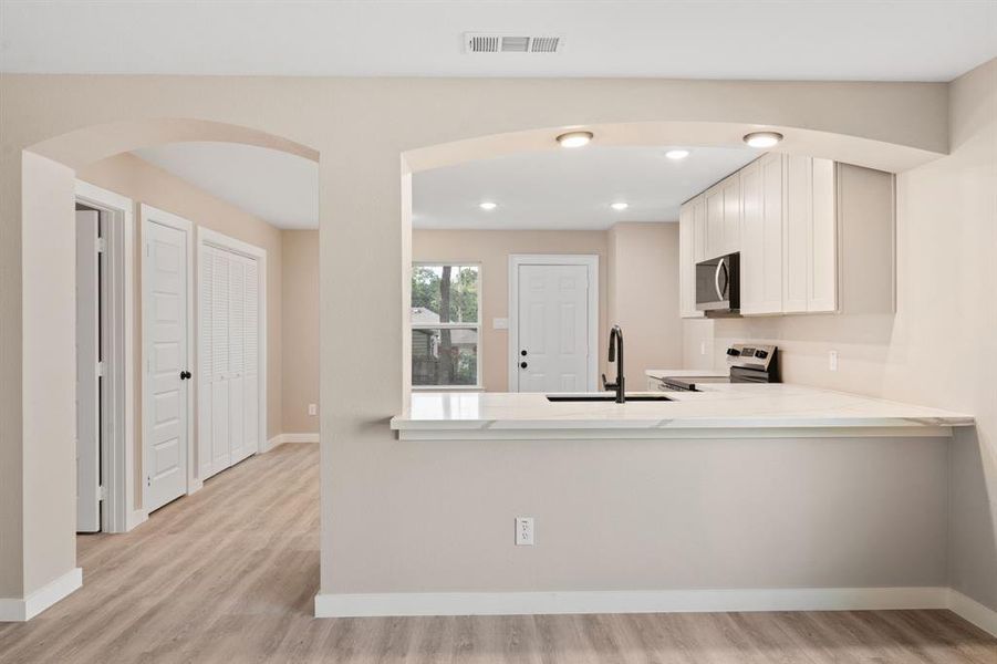 Kitchen featuring light stone countertops, white cabinets, appliances with stainless steel finishes, light wood-style floors, and arched walkways
