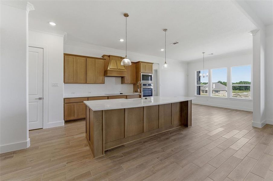 Open-concept kitchen featuring an oversized island with pendant lighting, wood-finish cabinetry, built-in double ovens, and tile flooring
