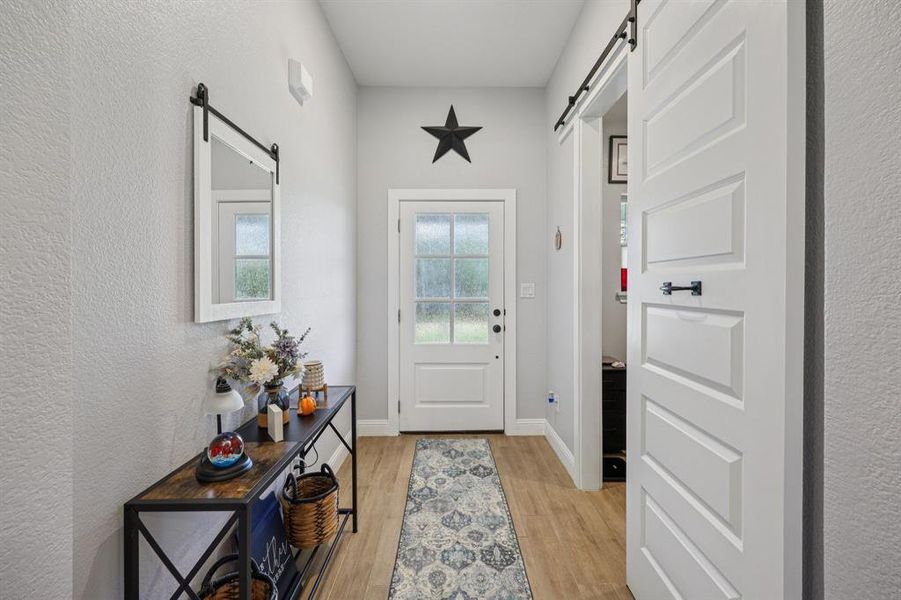 Doorway to outside with a barn door, a textured wall, and wood finished floors Doorway to outside with a barn door, a textured wall, and wood finished floors