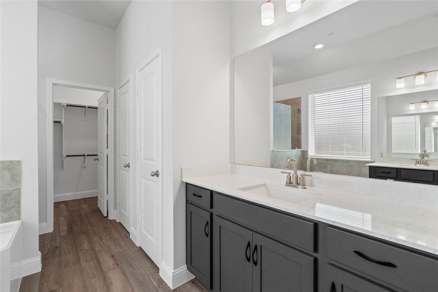 This elegant primary bathroom features a stylish dual-vanity layout with stained wood cabinetry, sleek brushed nickel fixtures, and mirrors. Bright quartz countertops and modern lighting create a fresh, upscale feel, while the space opens seamlessly to the primary walk-in closet, enhancing both flow and functionality. This elegant primary bathroom features a stylish dual-vanity layout with stained wood cabinetry, sleek brushed nickel fixtures, and mirrors. Bright quartz countertops and modern lighting create a fresh, upscale feel, while the space opens seamlessly to the primary walk-in closet, enhancing both flow and functionality.
