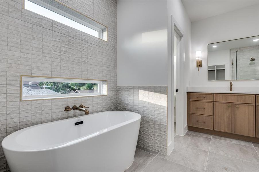 Bathroom featuring healthy amount of natural light, vanity, a freestanding tub, tile patterned flooring, and tile walls