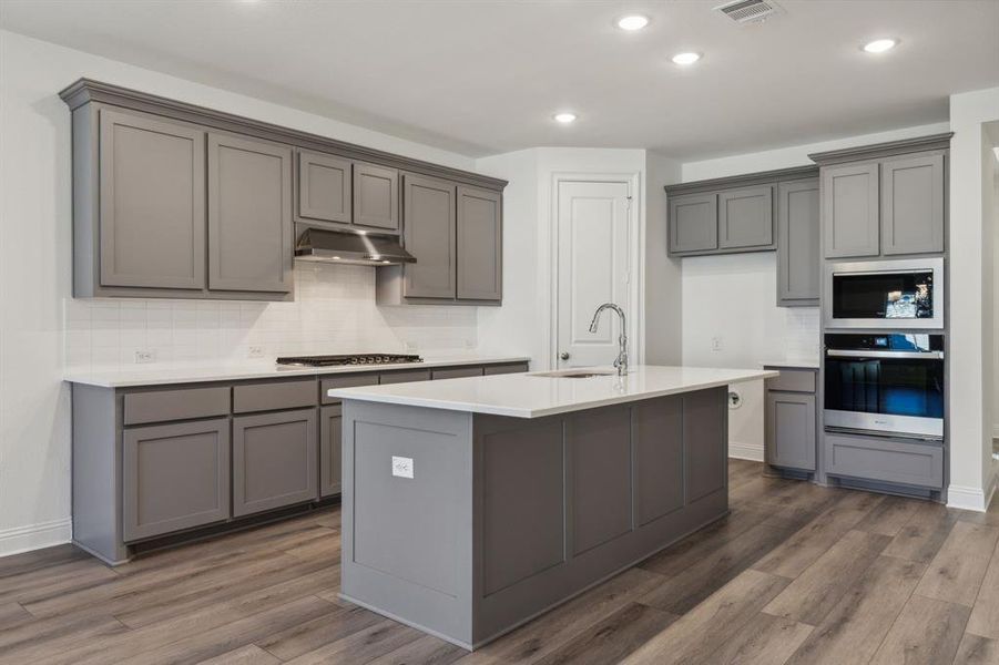 Kitchen with gray cabinetry, dark hardwood / wood-style floors, stainless steel appliances, and a kitchen island with sink