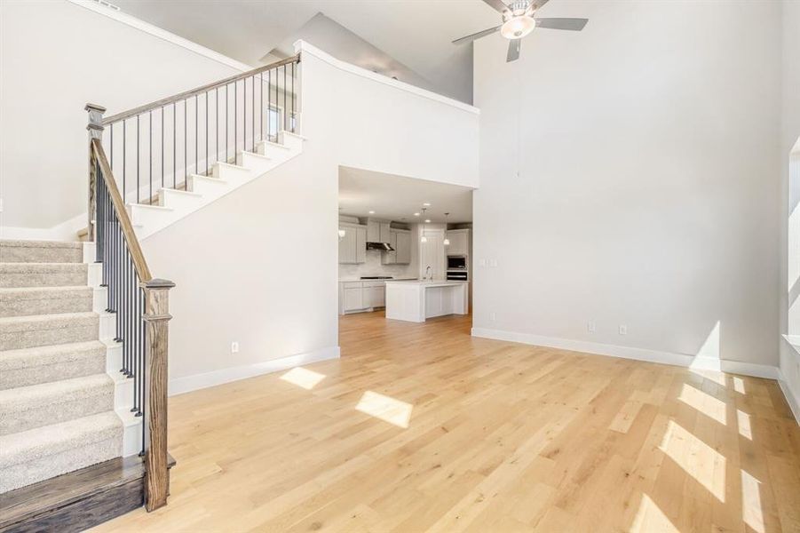Unfurnished living room with light wood finished floors, ceiling fan, and a high ceiling