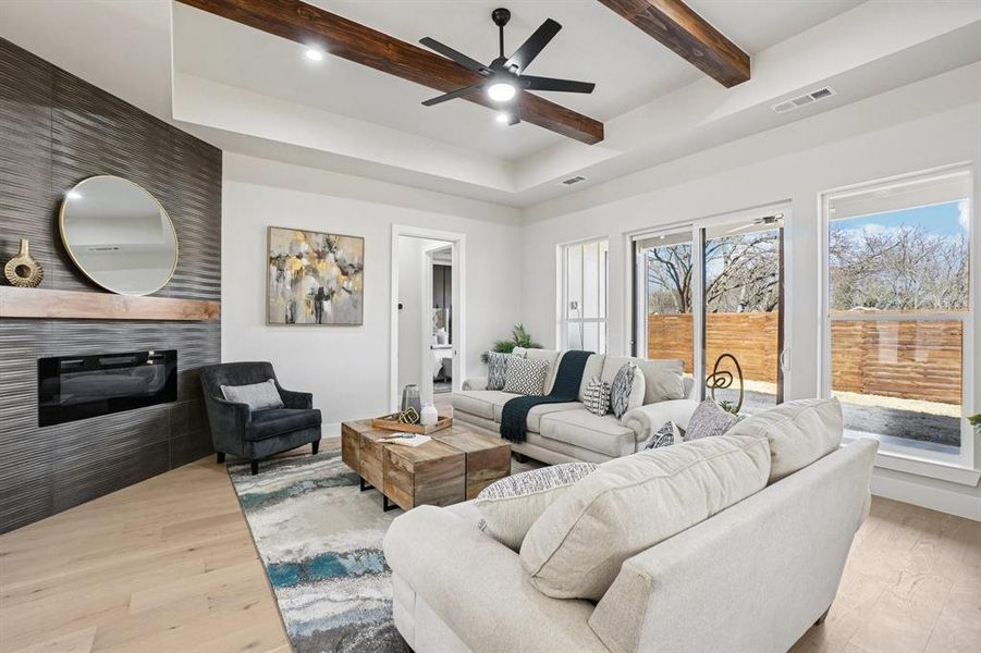 Living room with a tile fireplace, a ceiling fan, light wood-style floors, recessed lighting, and beamed ceiling