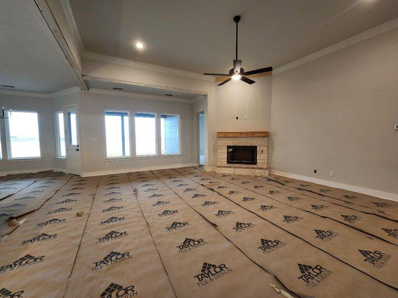 Unfurnished living room featuring a stone fireplace, crown molding, and a ceiling fan