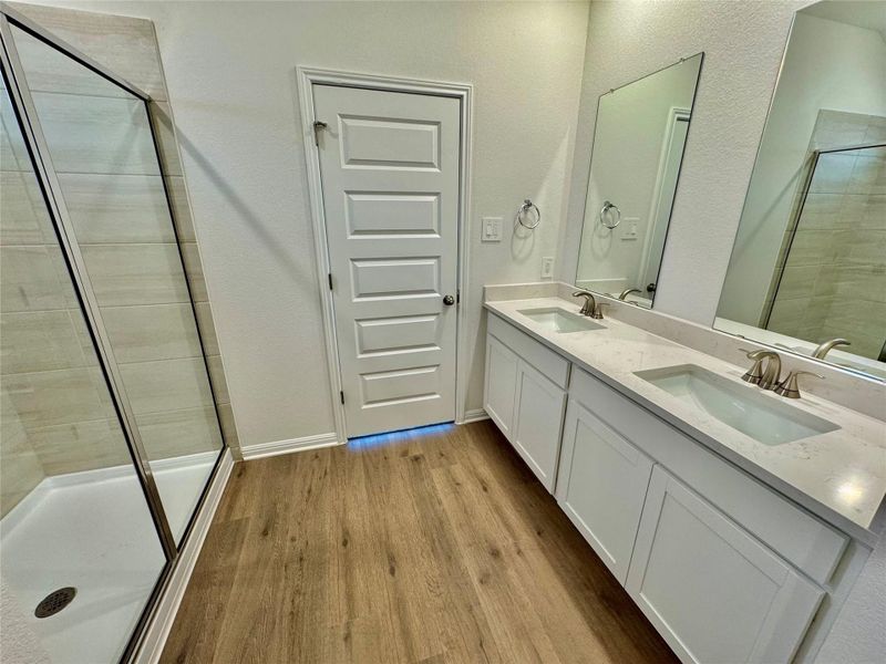 Full bathroom featuring a shower stall, double vanity, and wood finished floors Full bathroom featuring a shower stall, double vanity, and wood finished floors