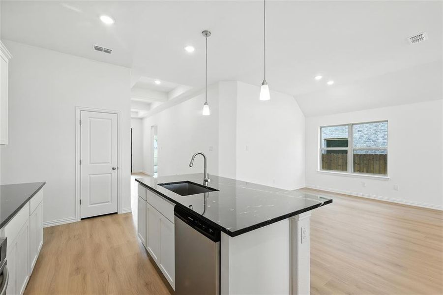 Kitchen with white cabinets, a center island with sink, dishwasher, light wood-style flooring, and lofted ceiling