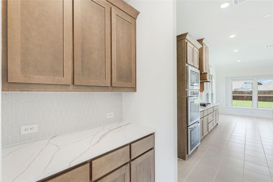 Kitchen with medium wood cabinets, quartz countertops, hexagon tile backsplash, and stainless steel appliances on tile floors