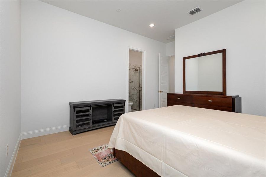 Bedroom with light wood-type flooring, connected bathroom, and recessed lighting