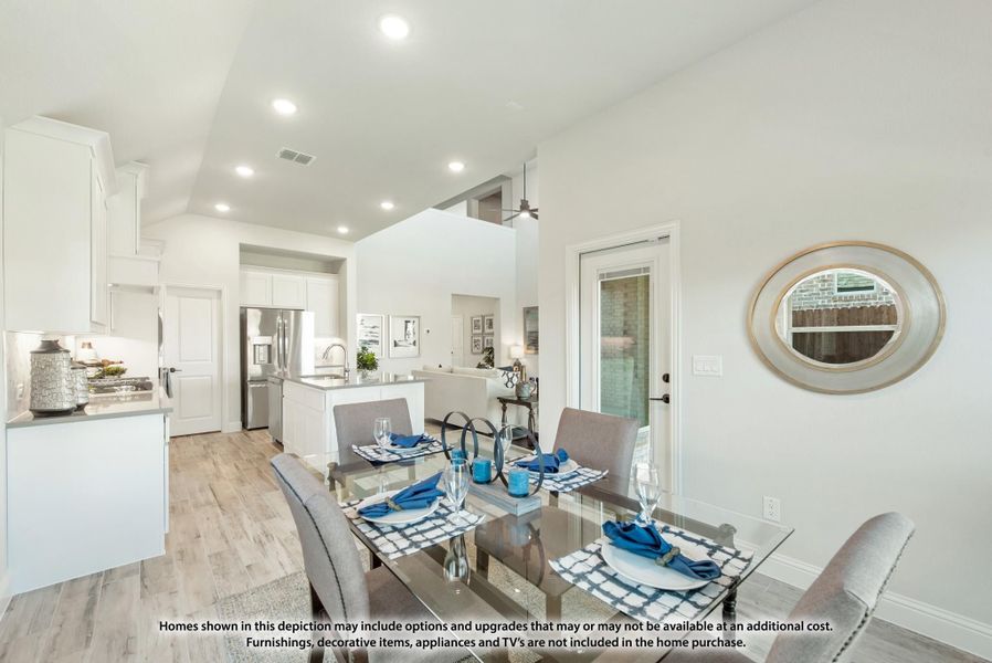 Open dining area with glass table and gray chairs, connected to white kitchen with island and hardwood floors