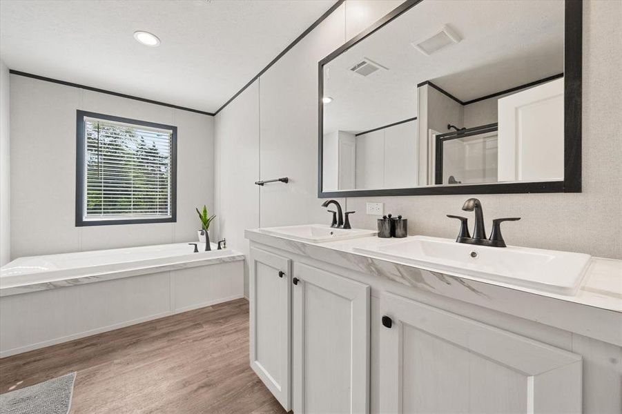 Bathroom featuring a double vanity with integrated sinks, black hardware, a built-in tub with a window, and wood-finish flooring Bathroom featuring a double vanity with integrated sinks, black hardware, a built-in tub with a window, and wood-finish flooring