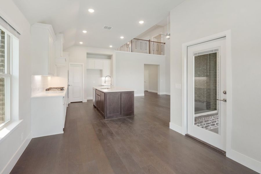 Open-concept kitchen with dark wood island, white cabinets, hardwood floors, and second-floor balcony overlook Open-concept kitchen with dark wood island, white cabinets, hardwood floors, and second-floor balcony overlook