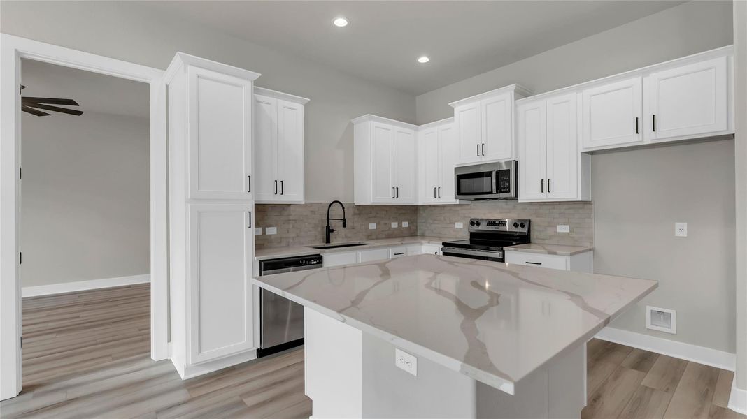 Kitchen featuring white cabinetry, a kitchen island, stainless steel appliances, light stone counters, and backsplash
