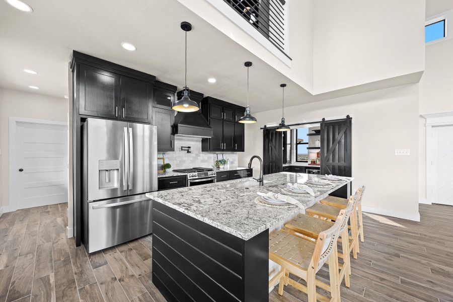 Kitchen with a barn door, dark cabinetry, appliances with stainless steel finishes, pendant lighting, and light stone countertops Kitchen with a barn door, dark cabinetry, appliances with stainless steel finishes, pendant lighting, and light stone countertops
