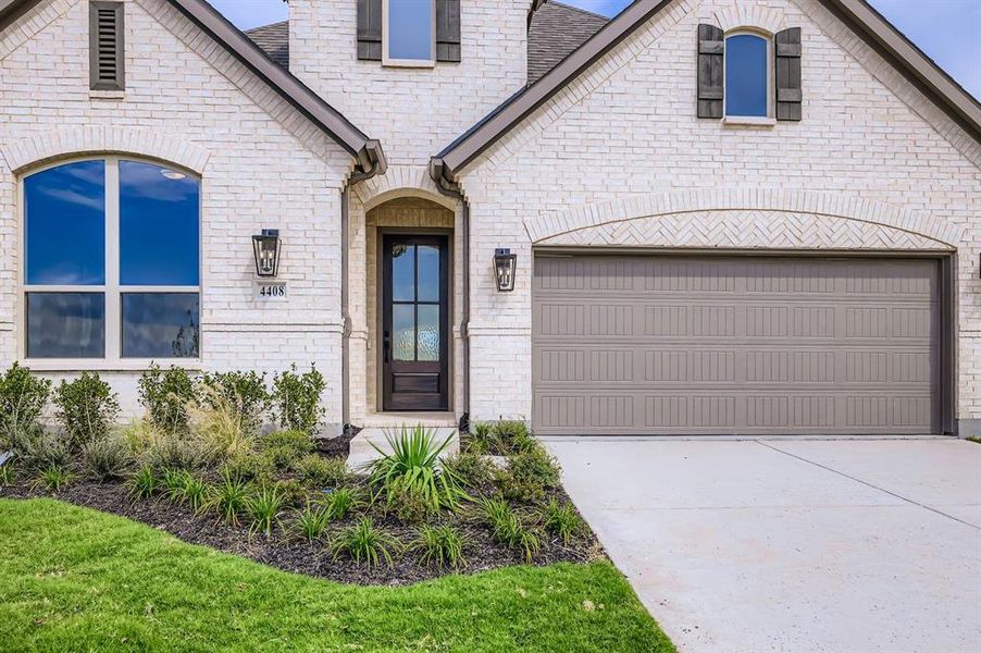 French country home featuring an attached garage, concrete driveway, brick siding, and roof with shingles French country home featuring an attached garage, concrete driveway, brick siding, and roof with shingles