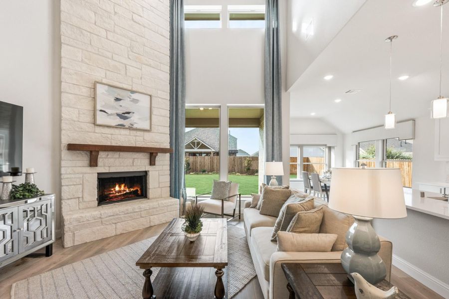 Living room with two-story stone fireplace, vaulted ceiling, hardwood floors, and large windows overlooking backyard Living room with two-story stone fireplace, vaulted ceiling, hardwood floors, and large windows overlooking backyard
