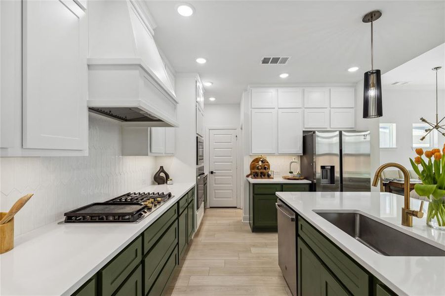 Kitchen featuring stainless steel appliances, visible vents, a sink, green cabinets, and custom range hood Kitchen featuring stainless steel appliances, visible vents, a sink, green cabinets, and custom range hood