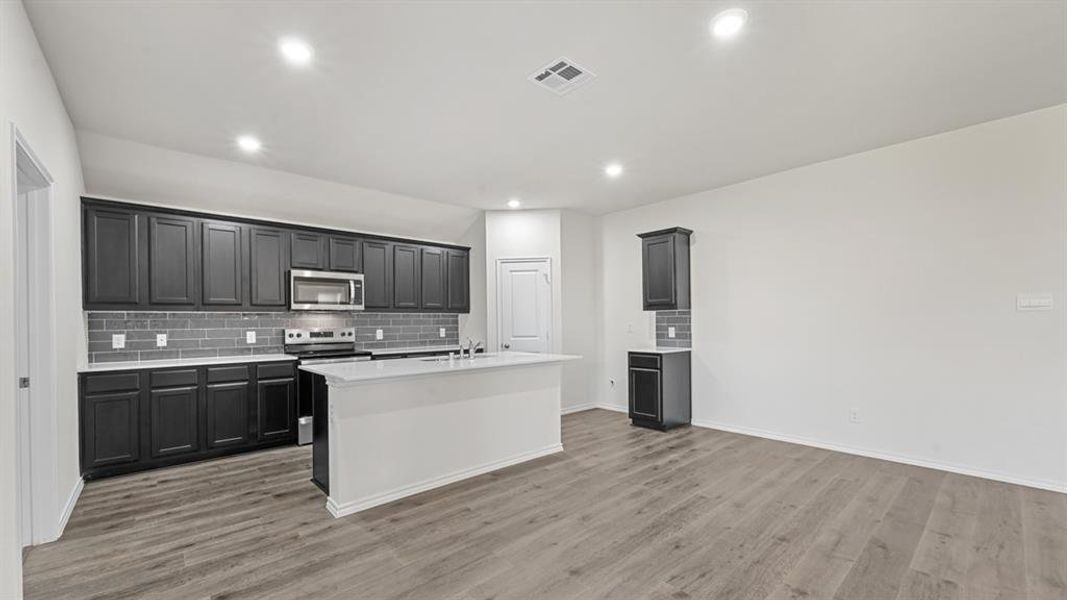 Modern kitchen featuring dark cabinetry, stainless steel appliances, a subway tile backsplash, and a central island with a sink