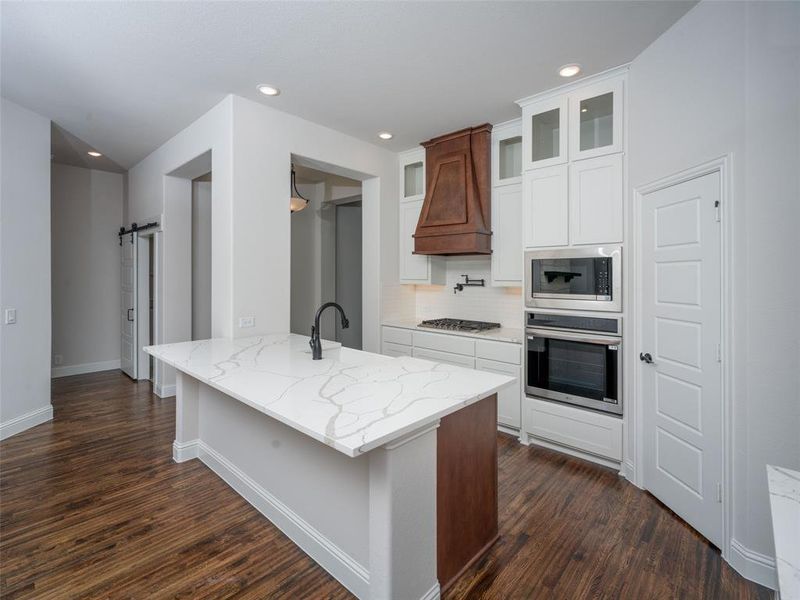 Kitchen featuring a barn door, light stone counters, tasteful backsplash, appliances with stainless steel finishes, and glass insert cabinets Kitchen featuring a barn door, light stone counters, tasteful backsplash, appliances with stainless steel finishes, and glass insert cabinets